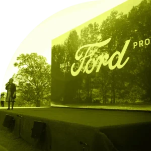 Photo of person speaking in front of large Ford sign