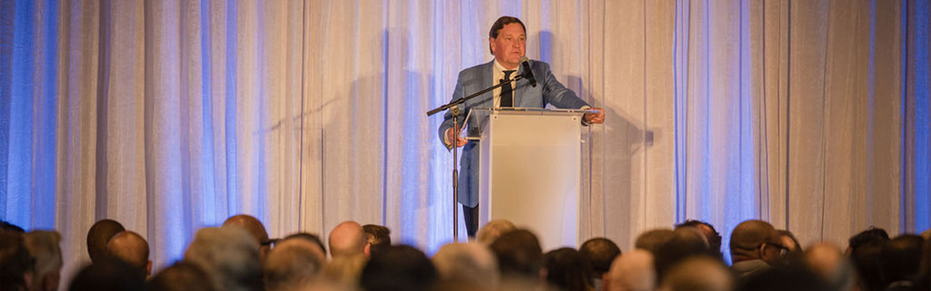 man at podium talking to crowd at event